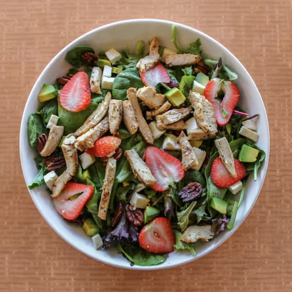 Overhead view of a fresh salad with grilled chicken, strawberries, avocado, and pecans.