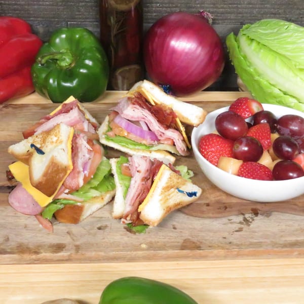 Club sandwiches with bacon, lettuce, tomato, and cheese, served with a fruit cup.