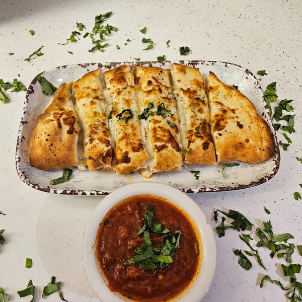 Cheesy garlic breadsticks, garnished with basil, served with a side of marinara sauce.